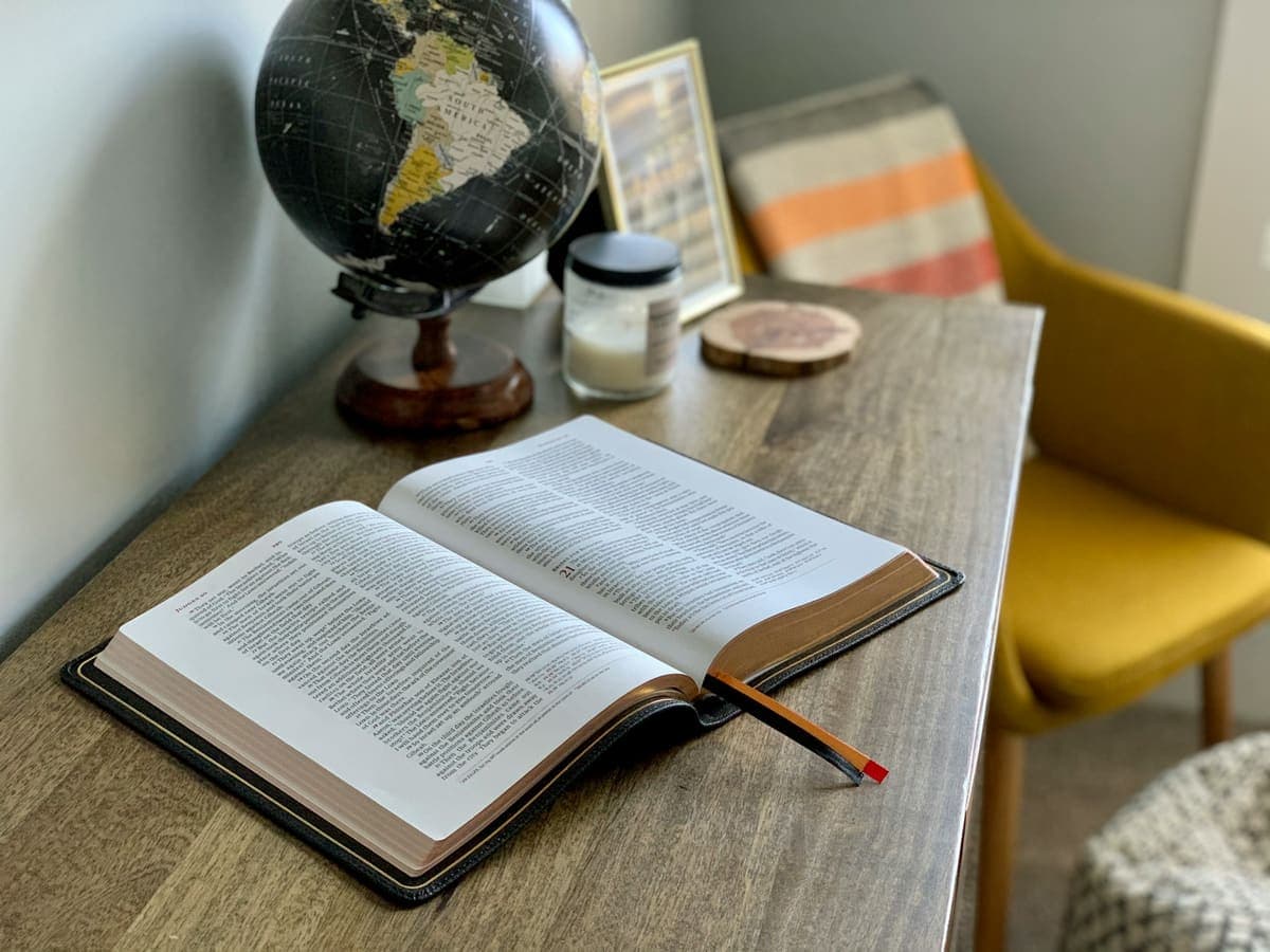 An open Bible on a study desk with a globe and candle